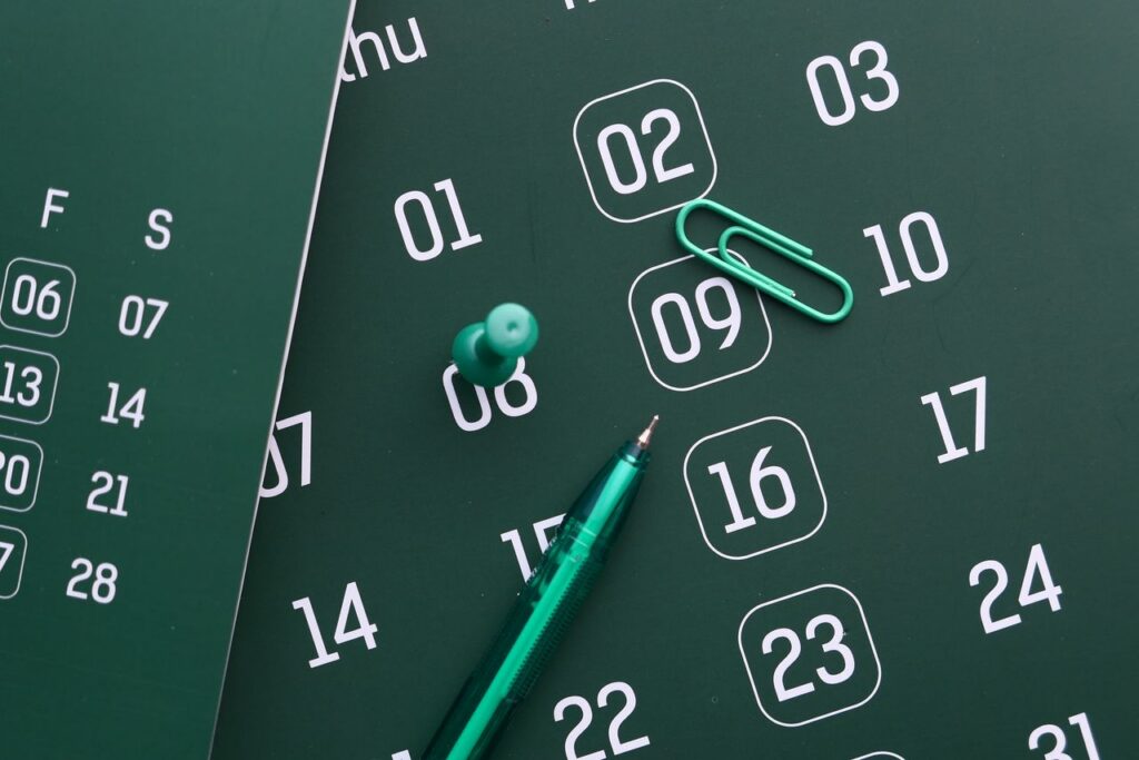 Home Close-up of a green calendar with pen, push pin, and paper clip for planning and organization.
