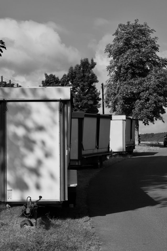 Home Monochrome image of trailers lined along a rural road under a bright sky.